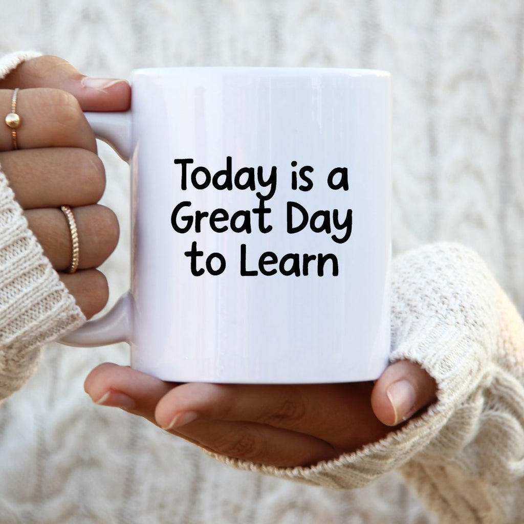 White mug with 'Today is a Great Day to Learn' text held by a person wearing a beige sweater.