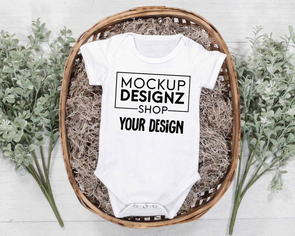 picture white onesie laid flat in a wicker basket with green plants