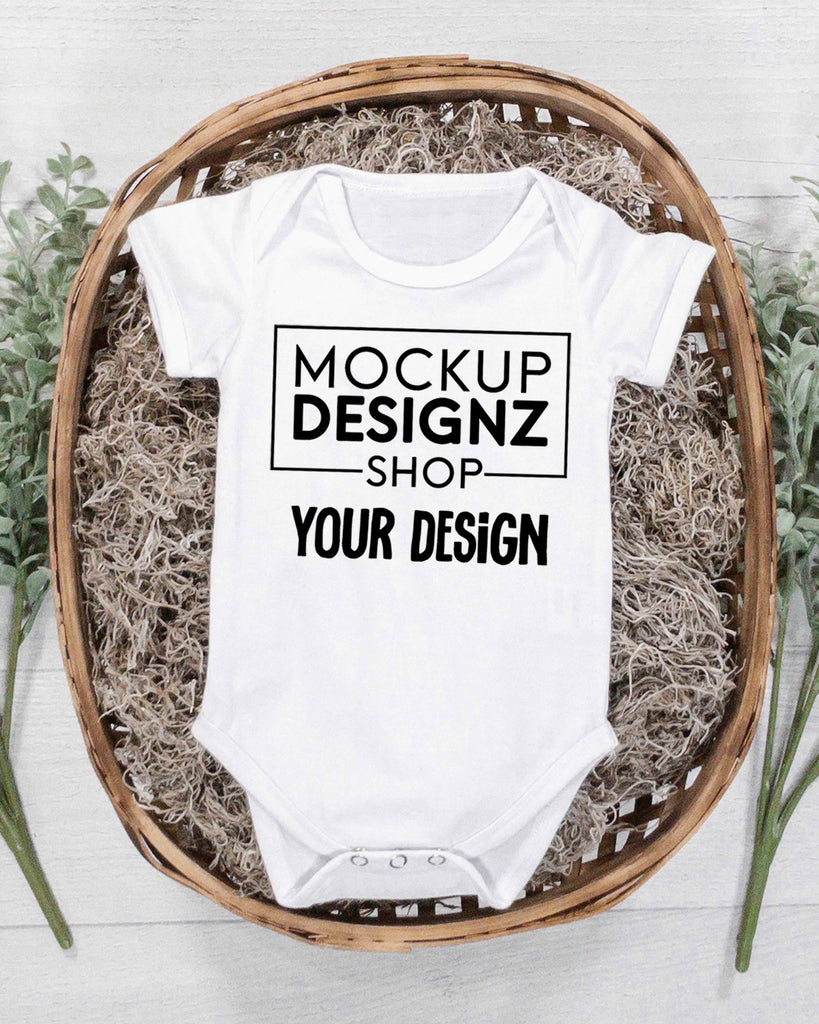 picture white onesie laid flat in a wicker basket with green plants portrait orientation