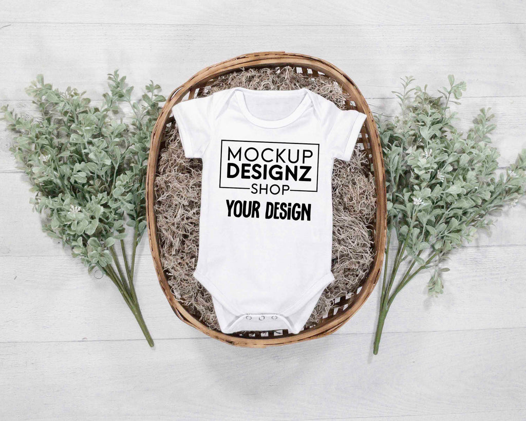 picture white onesie laid flat in a wicker basket with green plants landscape orientation zoomed out